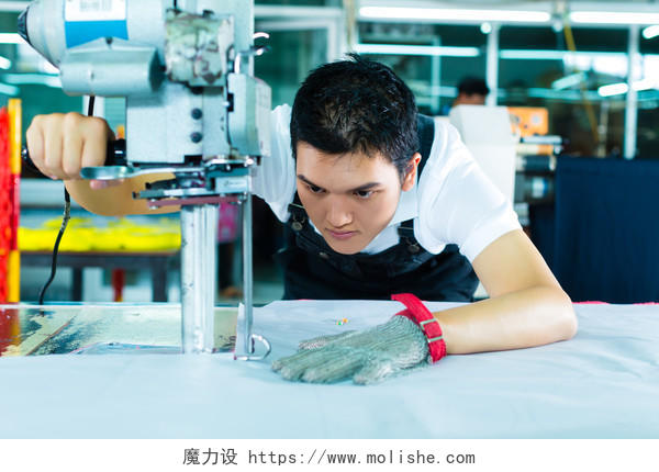 在中国的一家纺织厂里一个工人他戴着一副手套正在工作那是一台用来切割布料的大机器技术工人